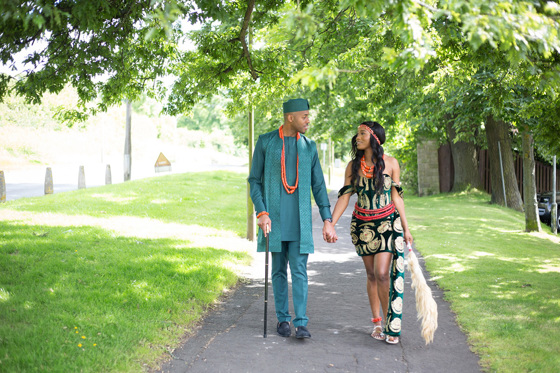 Bride and groom in traditional Nigerian clothing holding hands and smiling at each other while walking along path